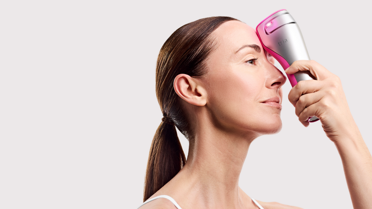 Woman using a Tria FRX device on her face against a light gray background